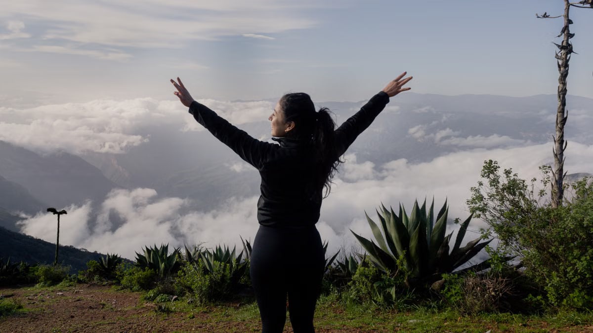 A woman with arms raised enjoying a scenic mountain view in Pinal de Amoles, Mexico.